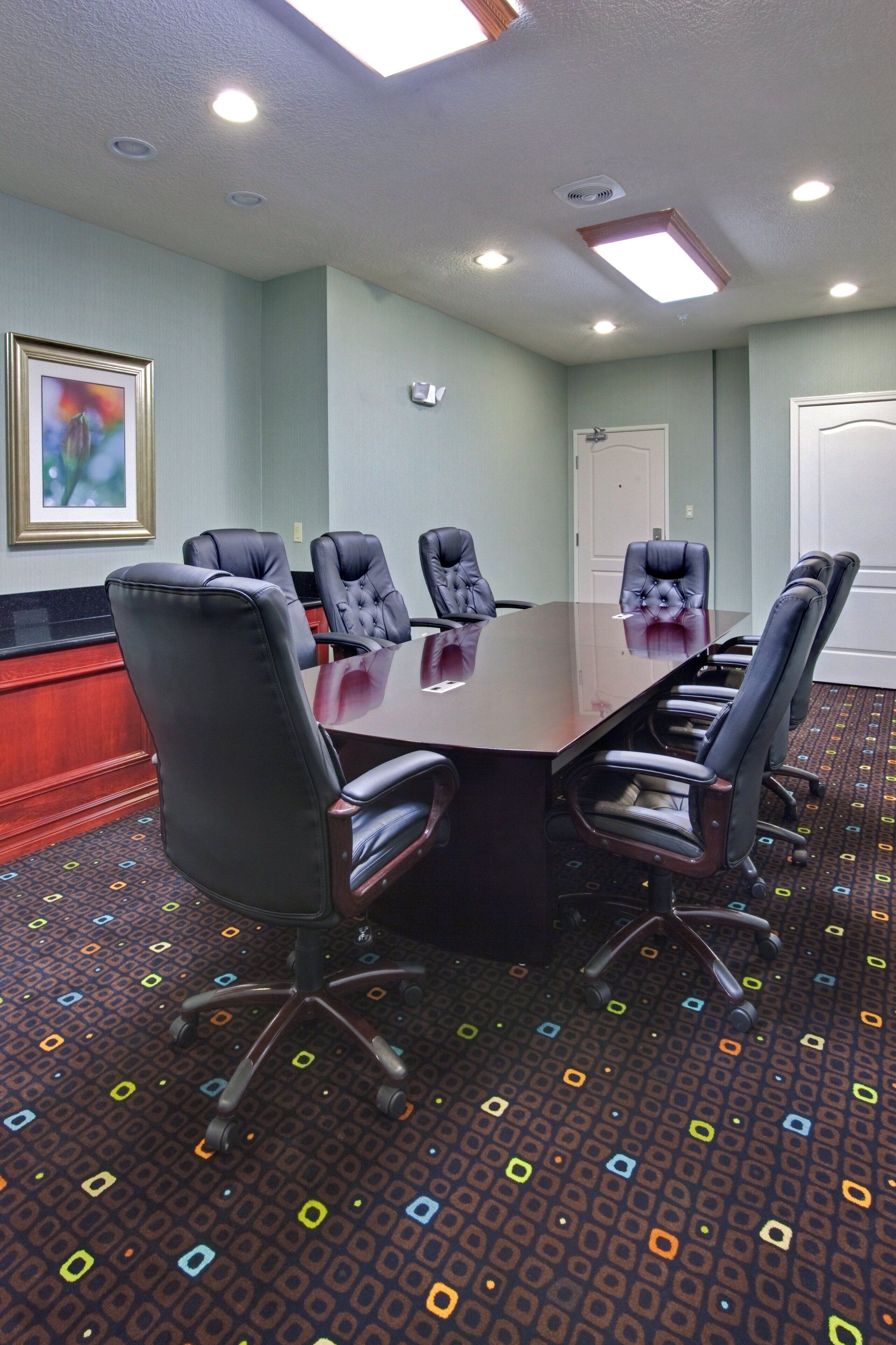 A conference room with a large table, six chairs, and a door in the background.
