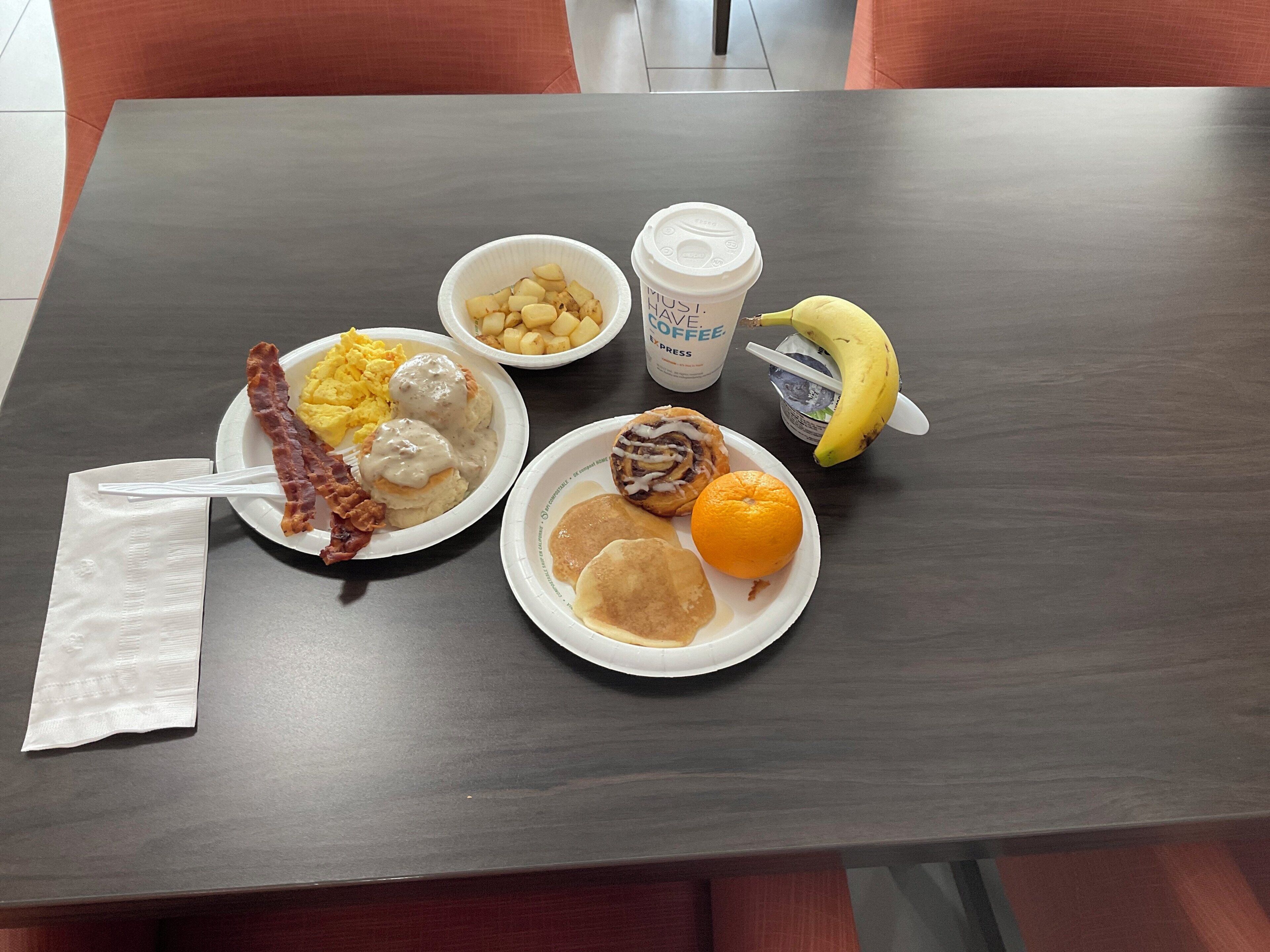 A table with breakfast items including eggs, sausage, biscuits, a banana, and a coffee cup.