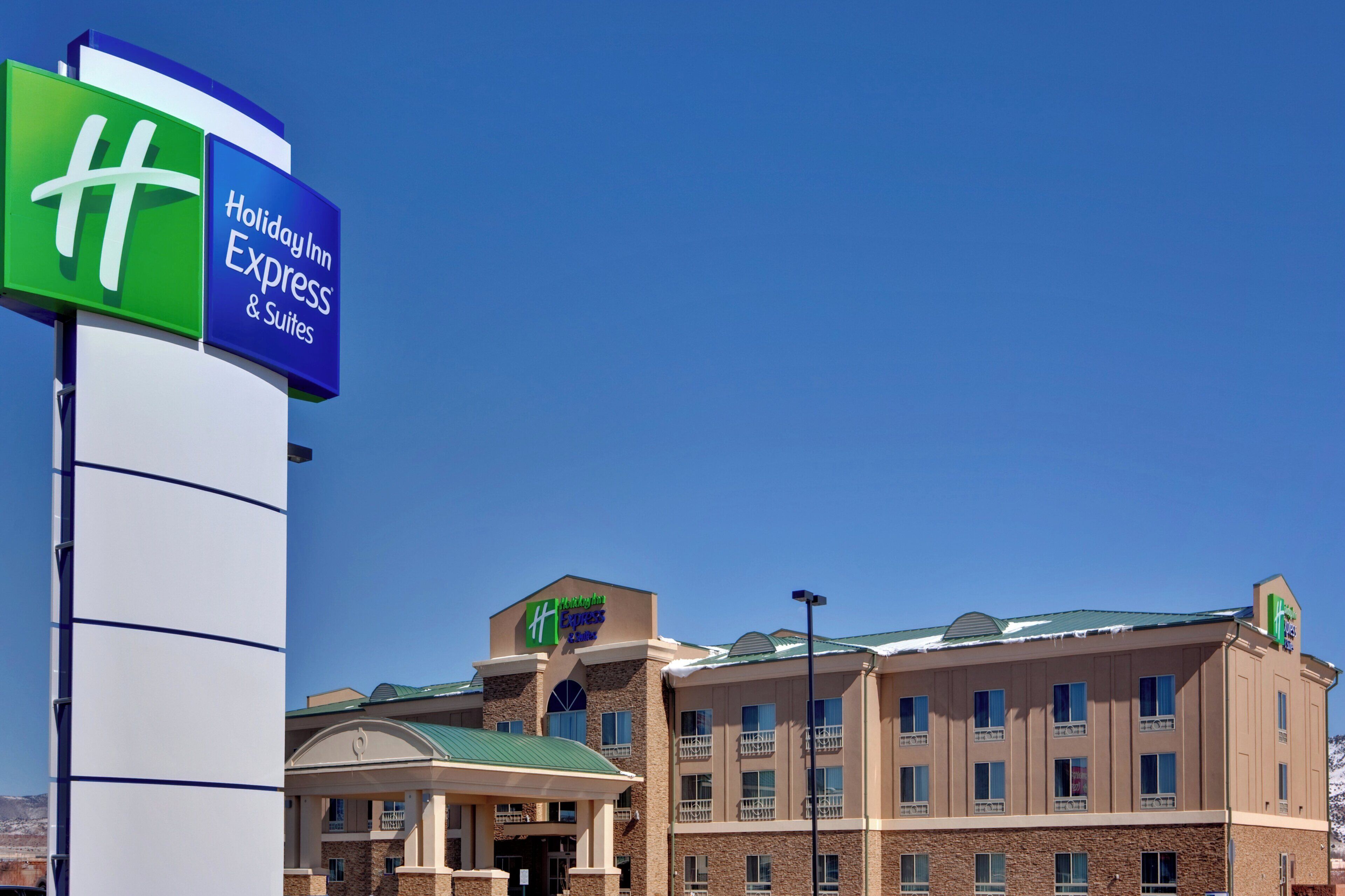 A Holiday Inn Express & Suites building with a prominent sign, a covered entrance, and a multi-story structure with a green roof.