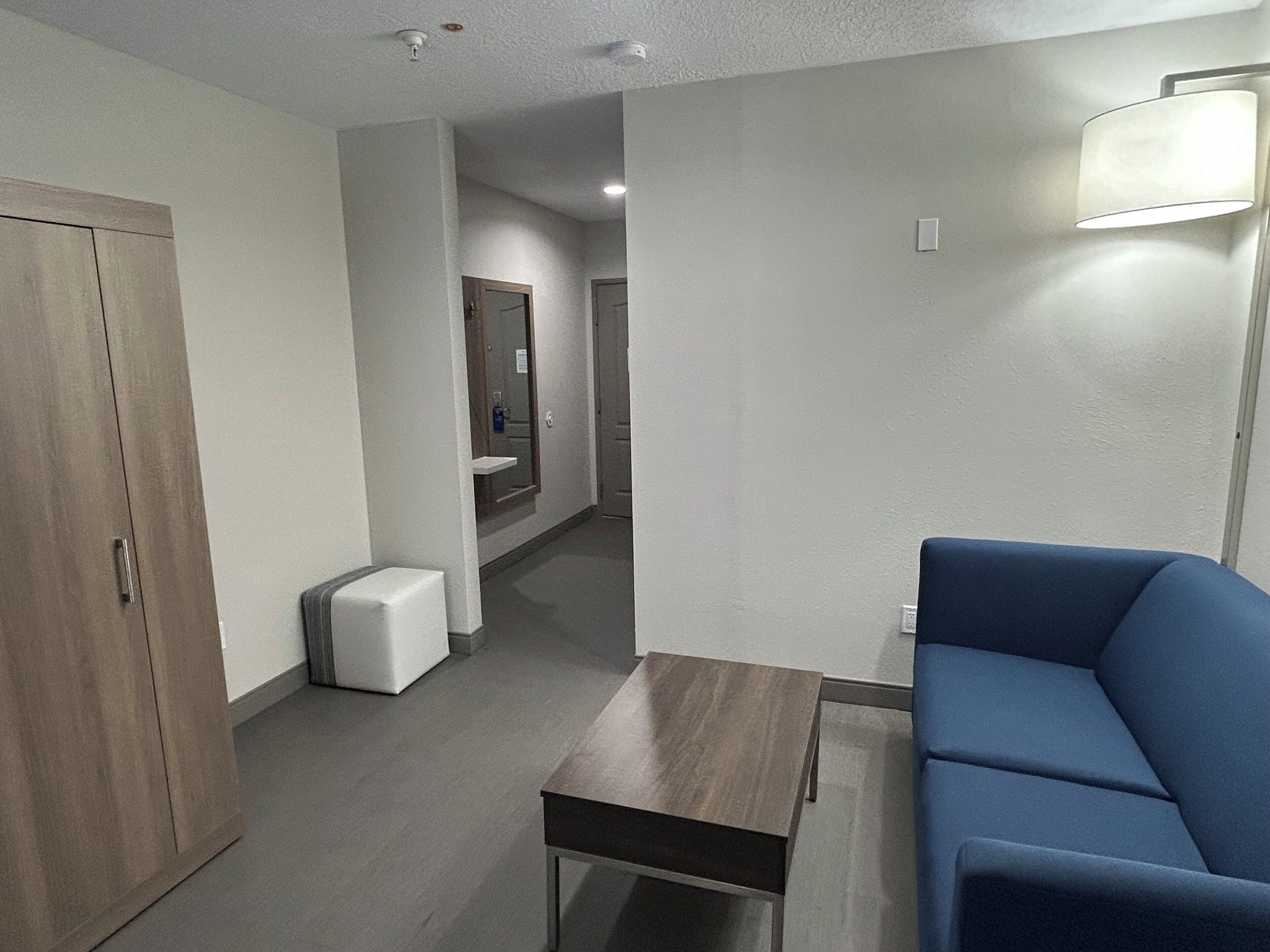 A modern hotel room with a wooden wardrobe, a small table, a blue sofa, and a mirror.