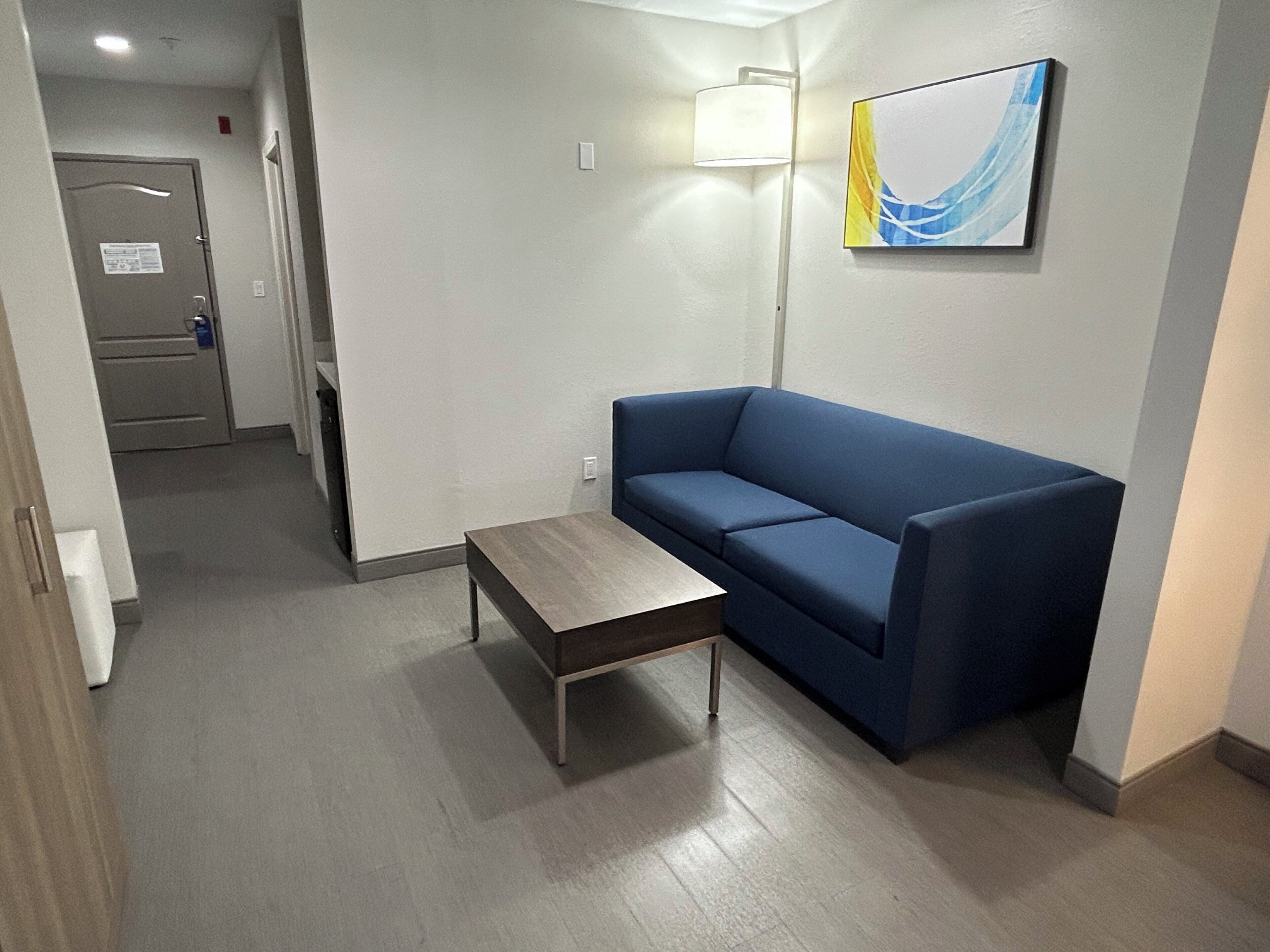 Een moderne hotelkamer met een blauwe bank, een klein houten tafeltje en een vloerlamp.