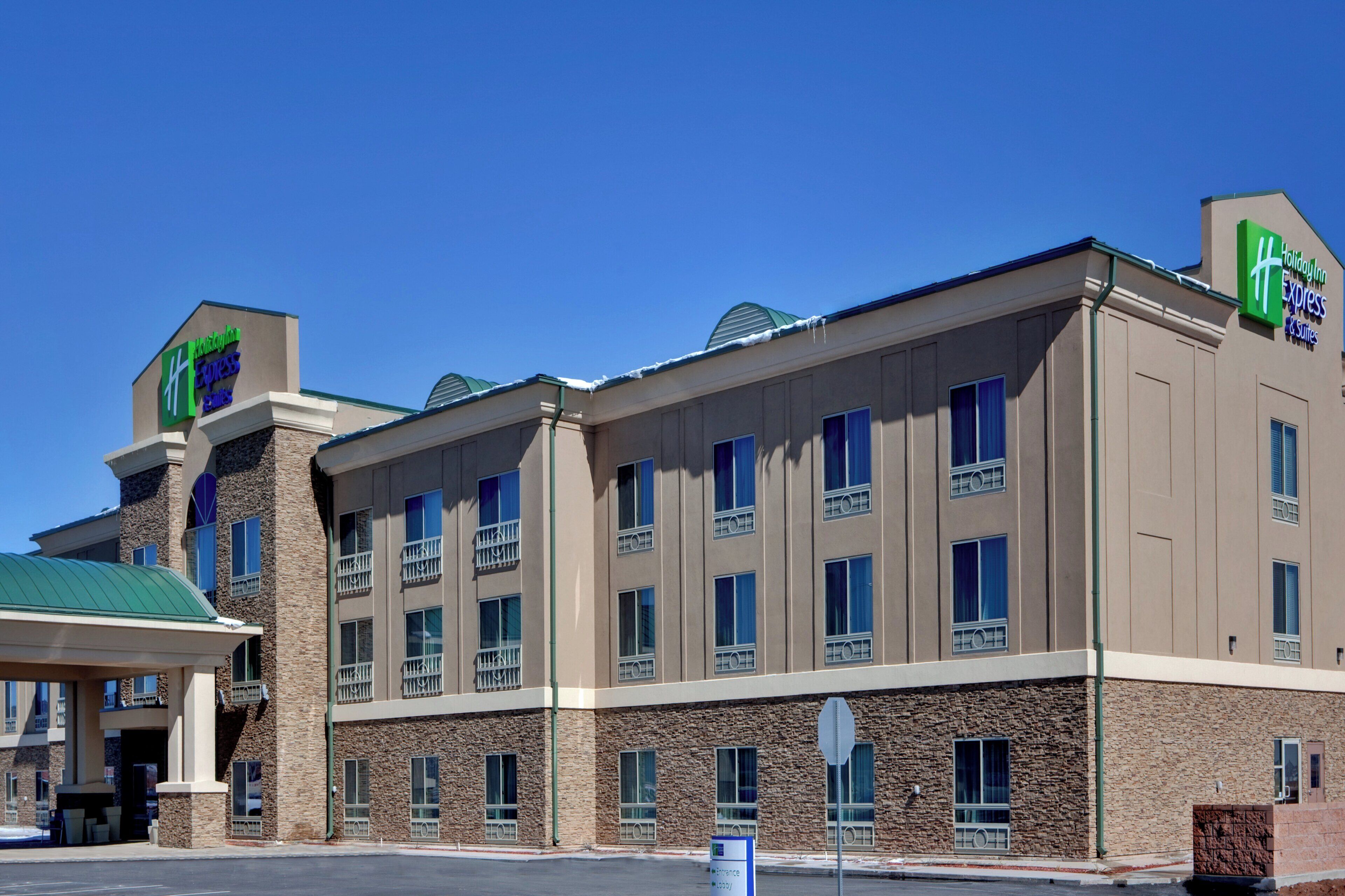 A Holiday Inn Express & Suites building with a stone facade, multiple windows, and a green roof.