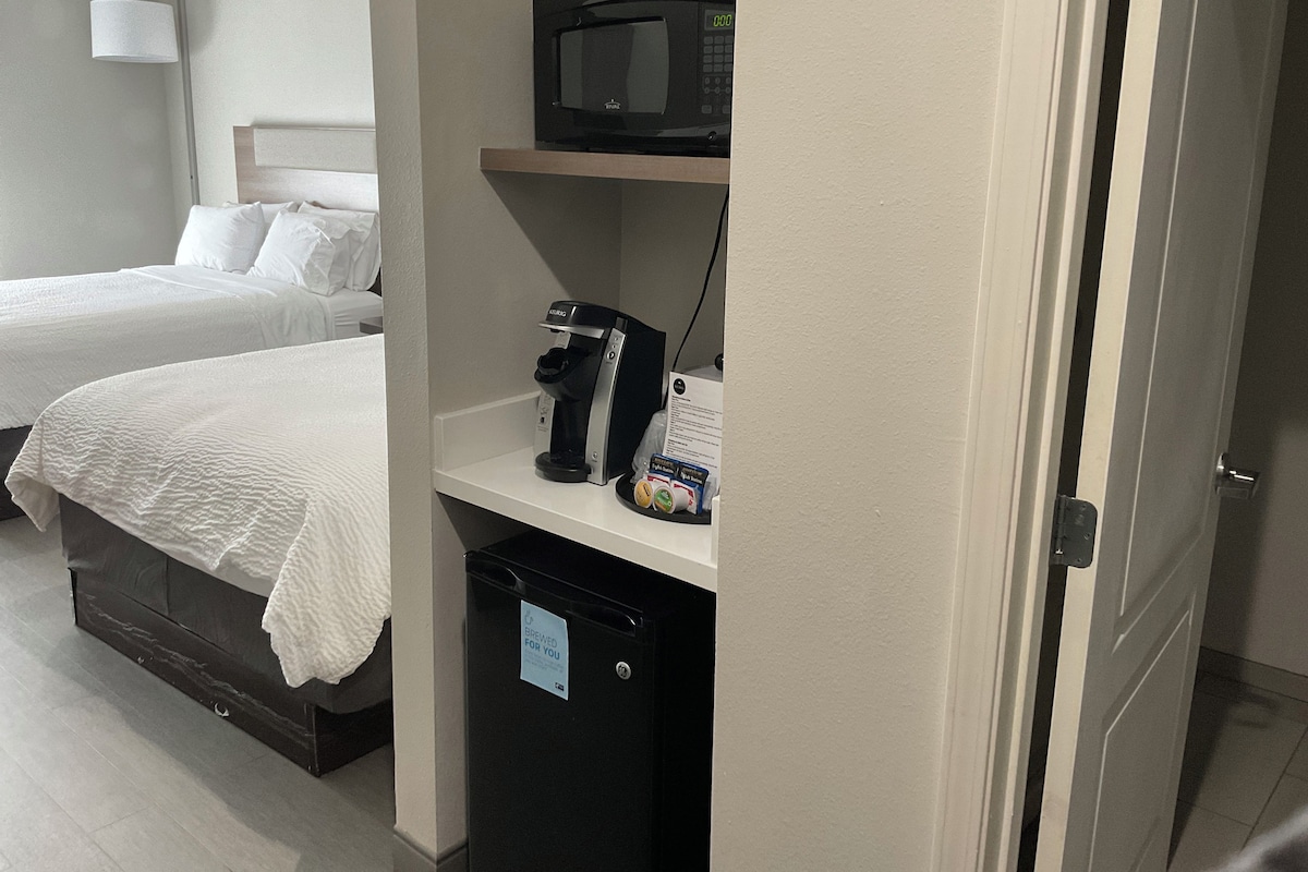 A hotel room with two beds, a microwave, a coffee machine, and a trash bin.
