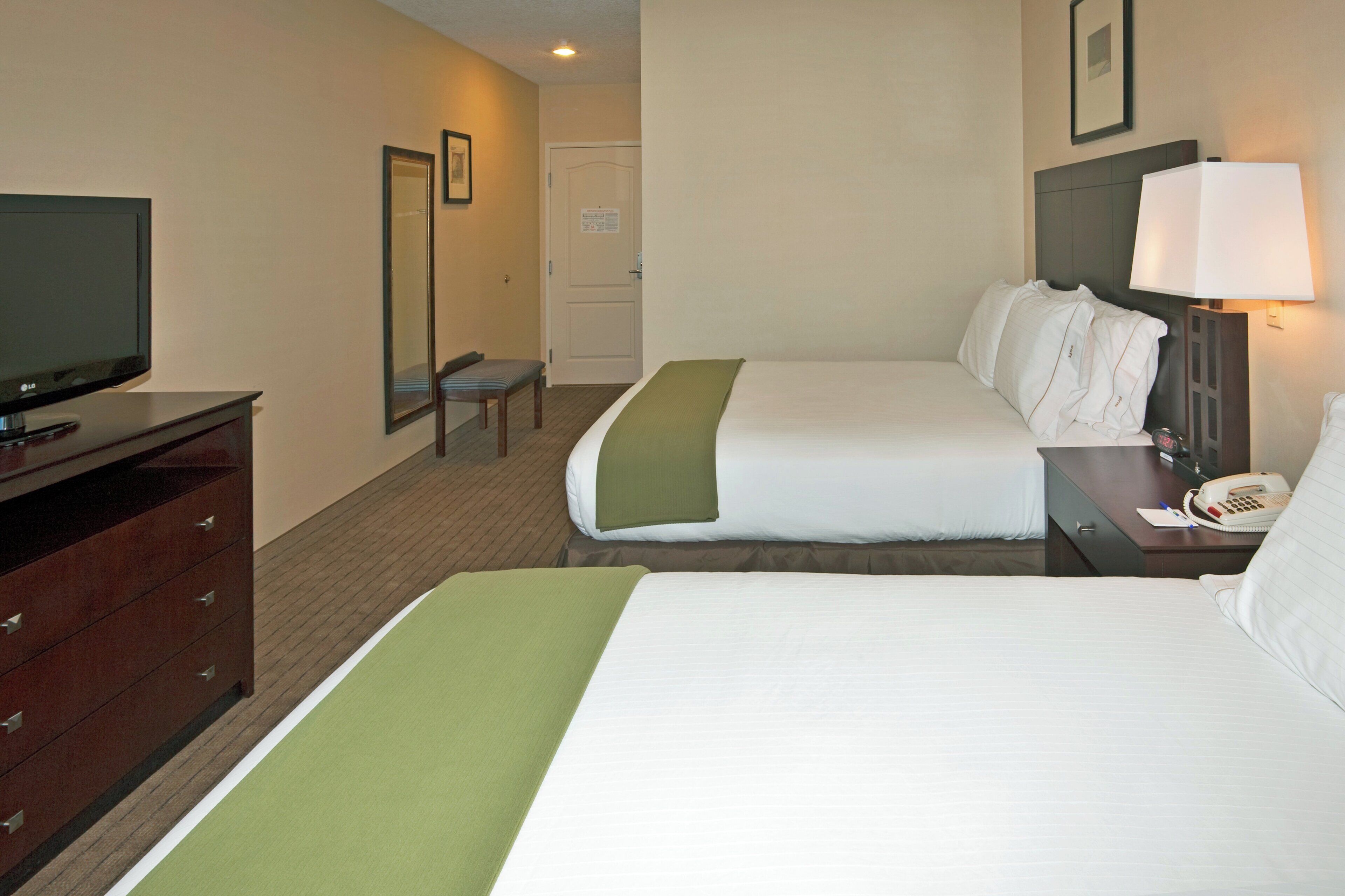 A hotel room with two beds, a television, a desk with a telephone, and a mirror.