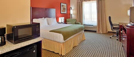 A hotel room with a bed, a desk, a microwave, a television, and a window with curtains.