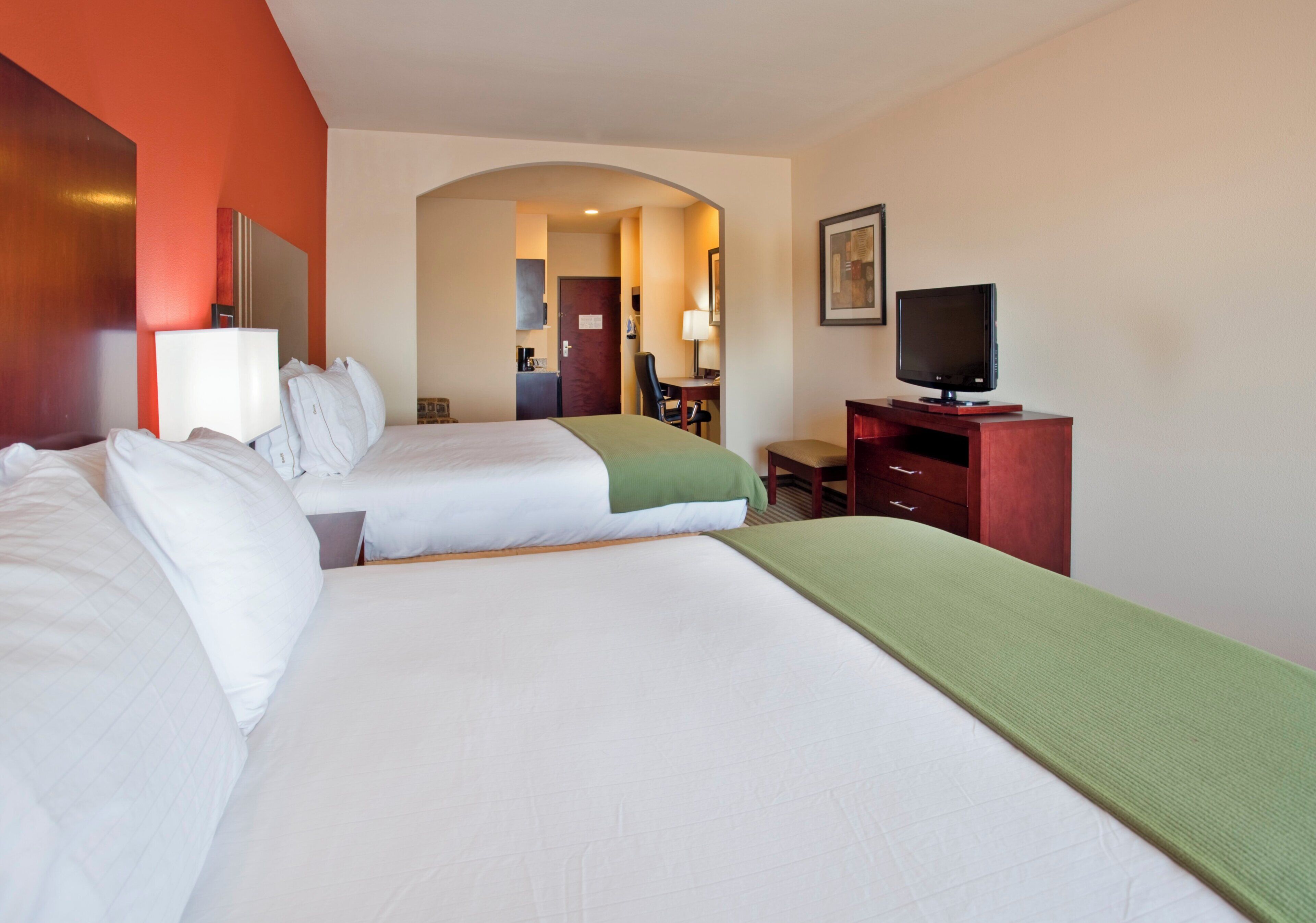 A hotel room with two beds, a television, a desk, and a mirror.