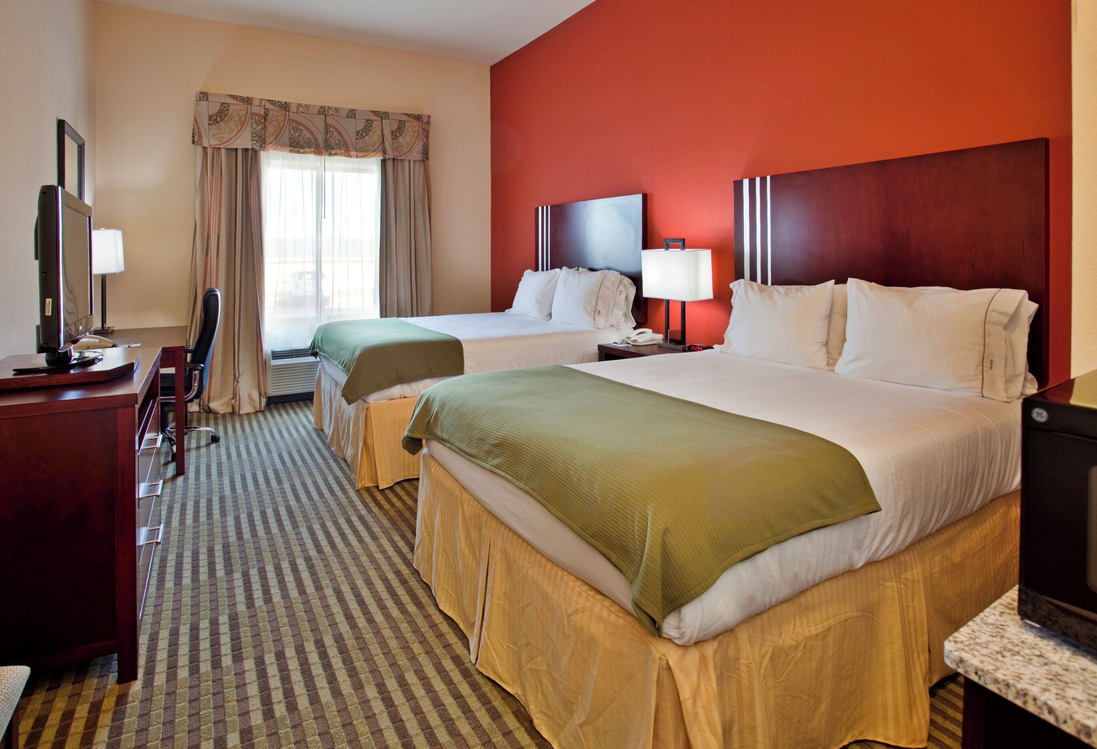 A hotel room with two beds, a desk with a computer, a chair, and a TV.