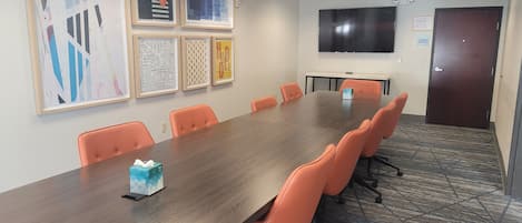 A conference room with a long table, orange chairs, a flat-screen TV, and framed artwork on the wall.