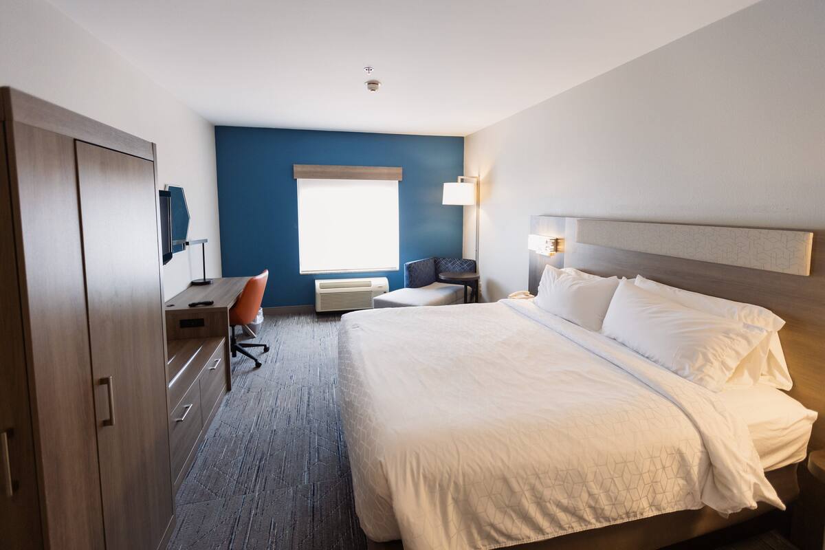 A hotel room with a large bed, a desk, a chair, a small table, and a window.