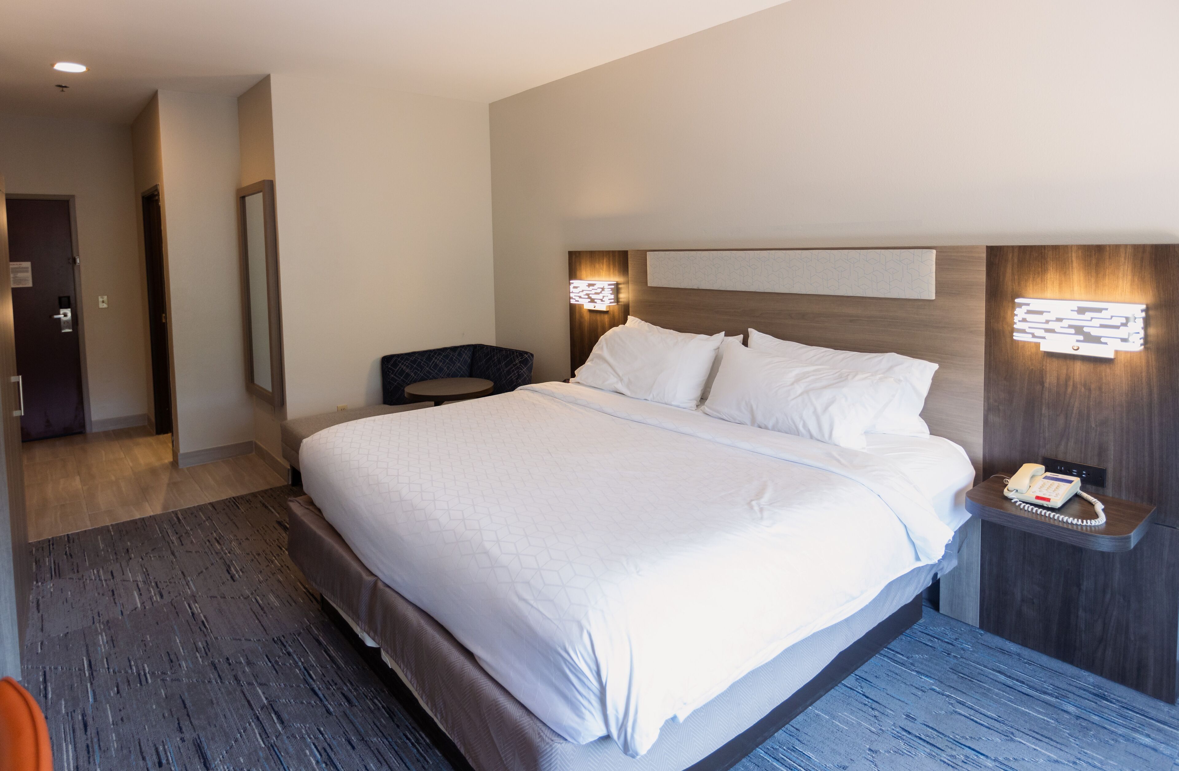Habitació d'hotel moderna amb un llit gran, una taula de nit amb un telèfon i una petita zona de seients.