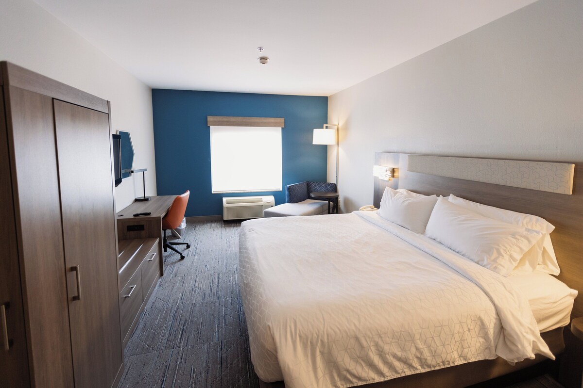 A hotel room with a bed, desk, chair, and a large window.