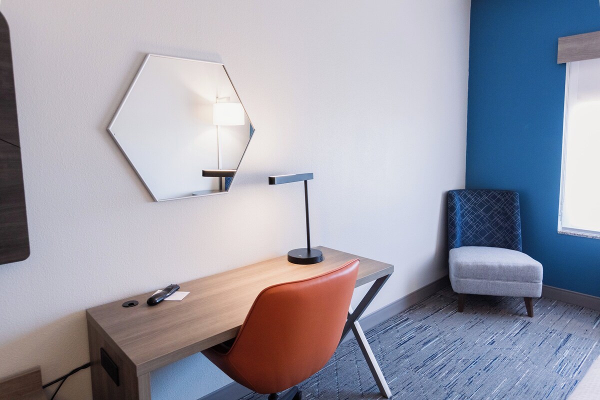 A hotel room with a desk, chair, and a large mirror on the wall.