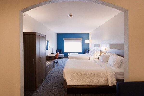 Ein Hotelzimmer mit zwei Betten, einem Schreibtisch, einem Stuhl, einem Kleiderschrank und einem großen Fenster.