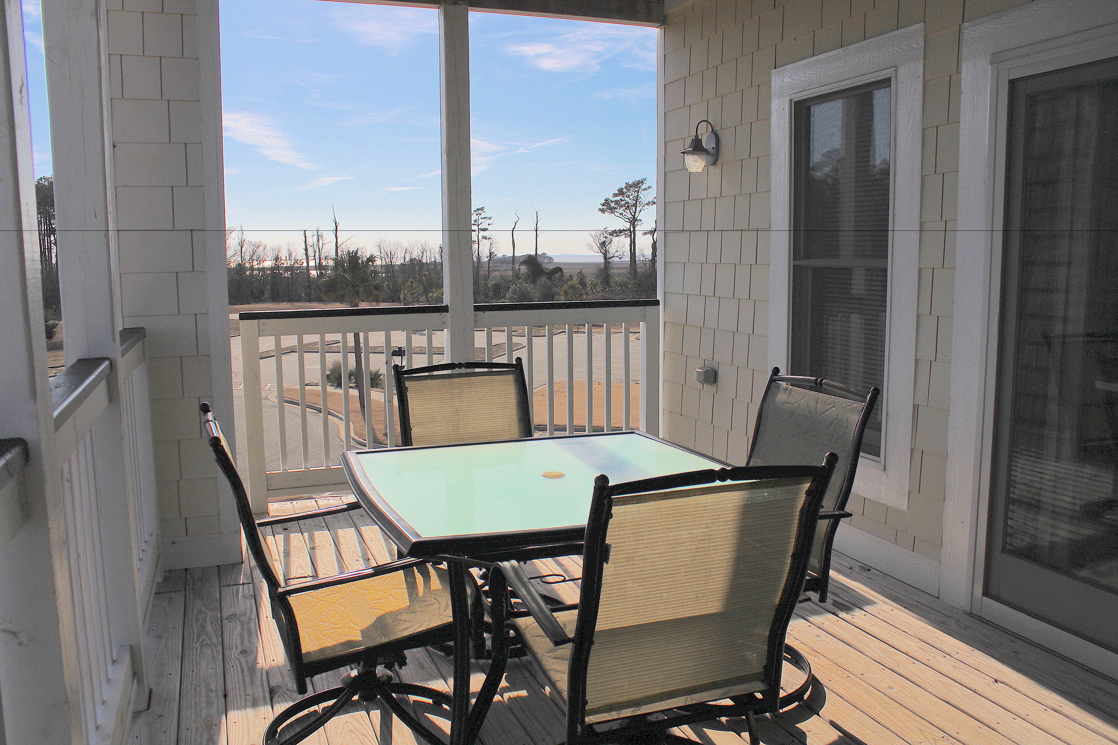 A covered patio with a table and chairs, a white fence, and a view of the landscape.