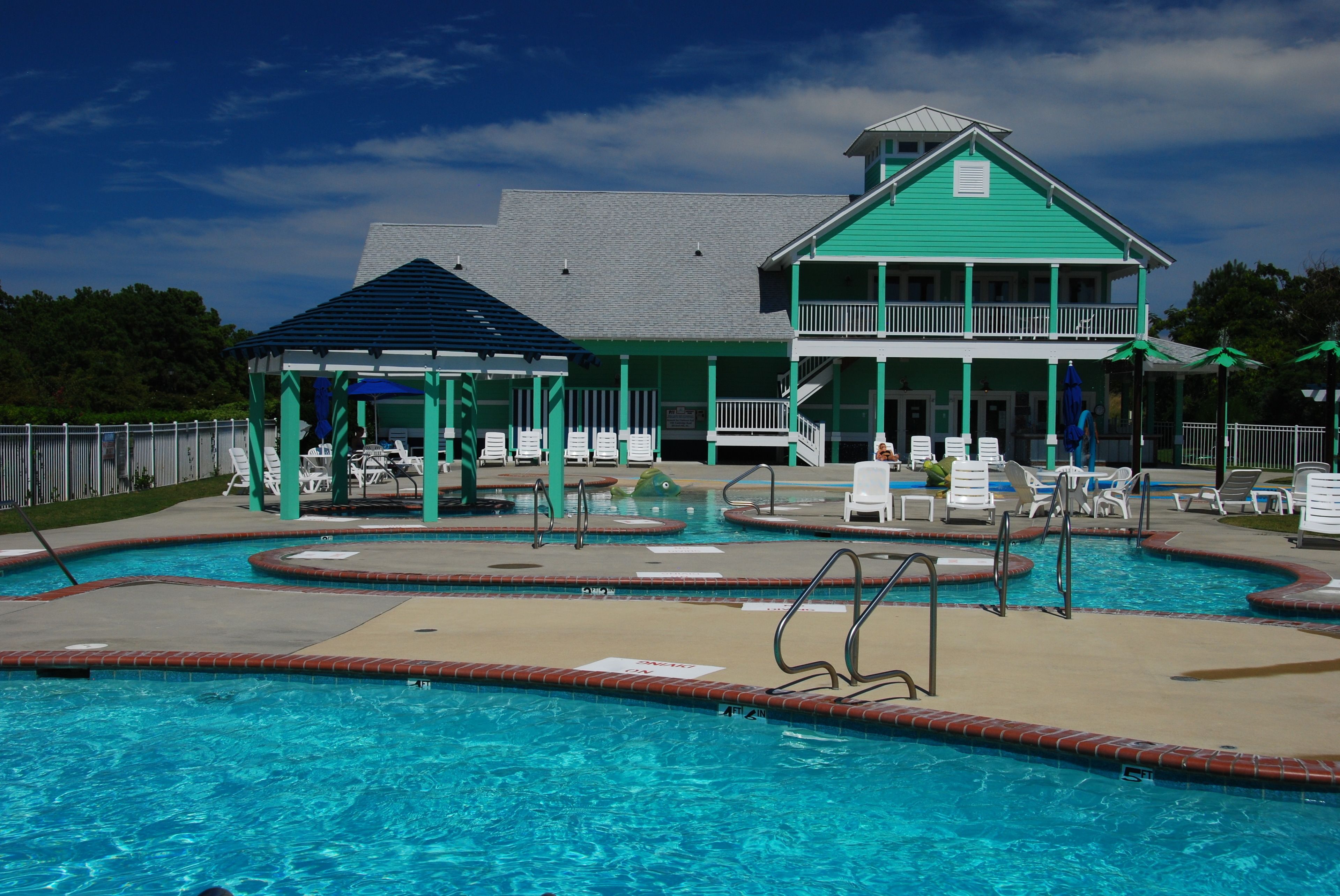 A pool area with a building featuring a green roof and a covered seating area with lounge chairs.