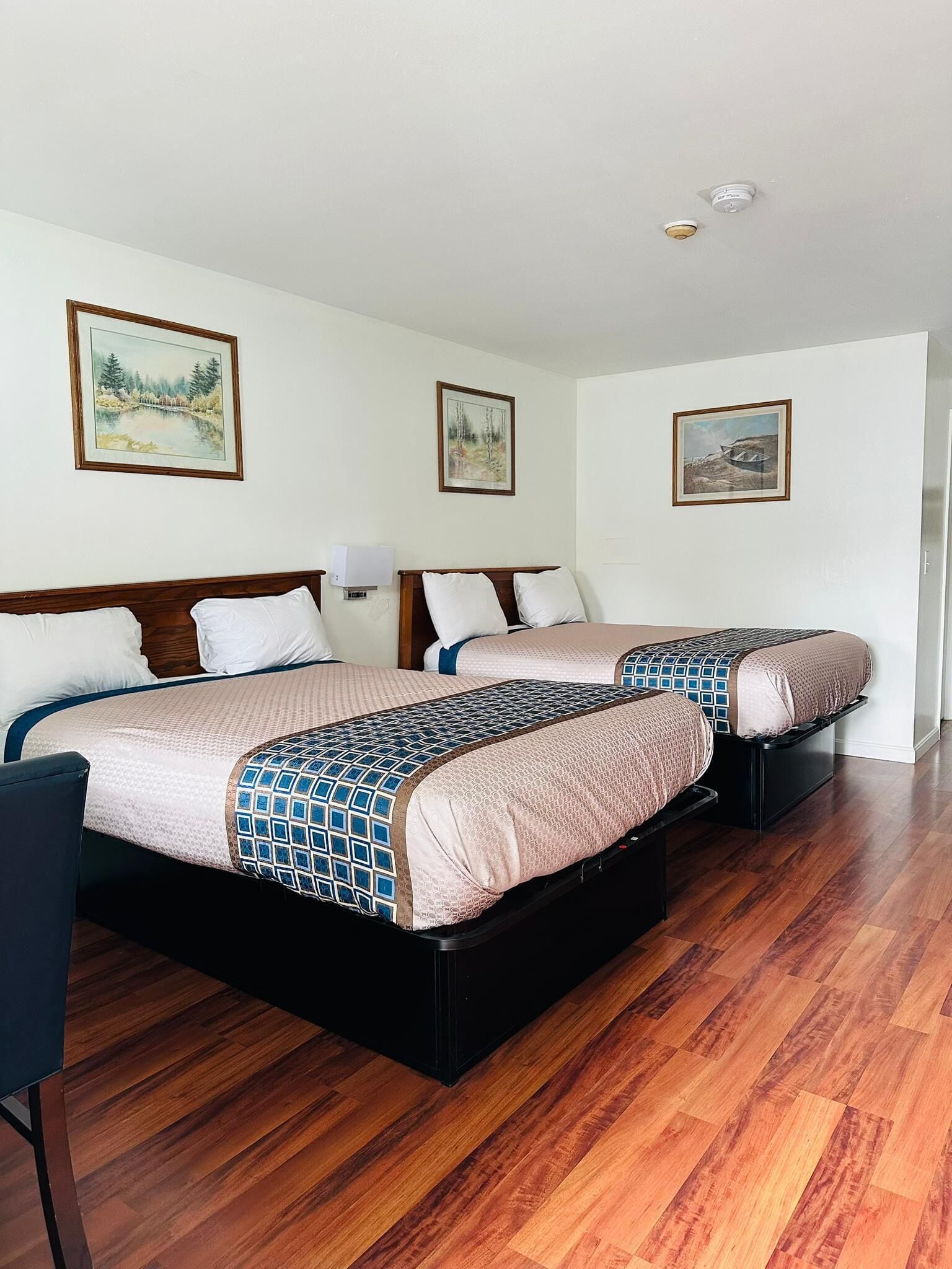 A hotel room with two beds, wooden flooring, and framed artwork on the walls.