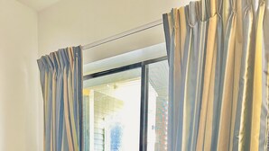 A room with a round table and two blue chairs, a window with striped curtains, and a view of a building outside. - Hampton Motor Inn (Hampton)