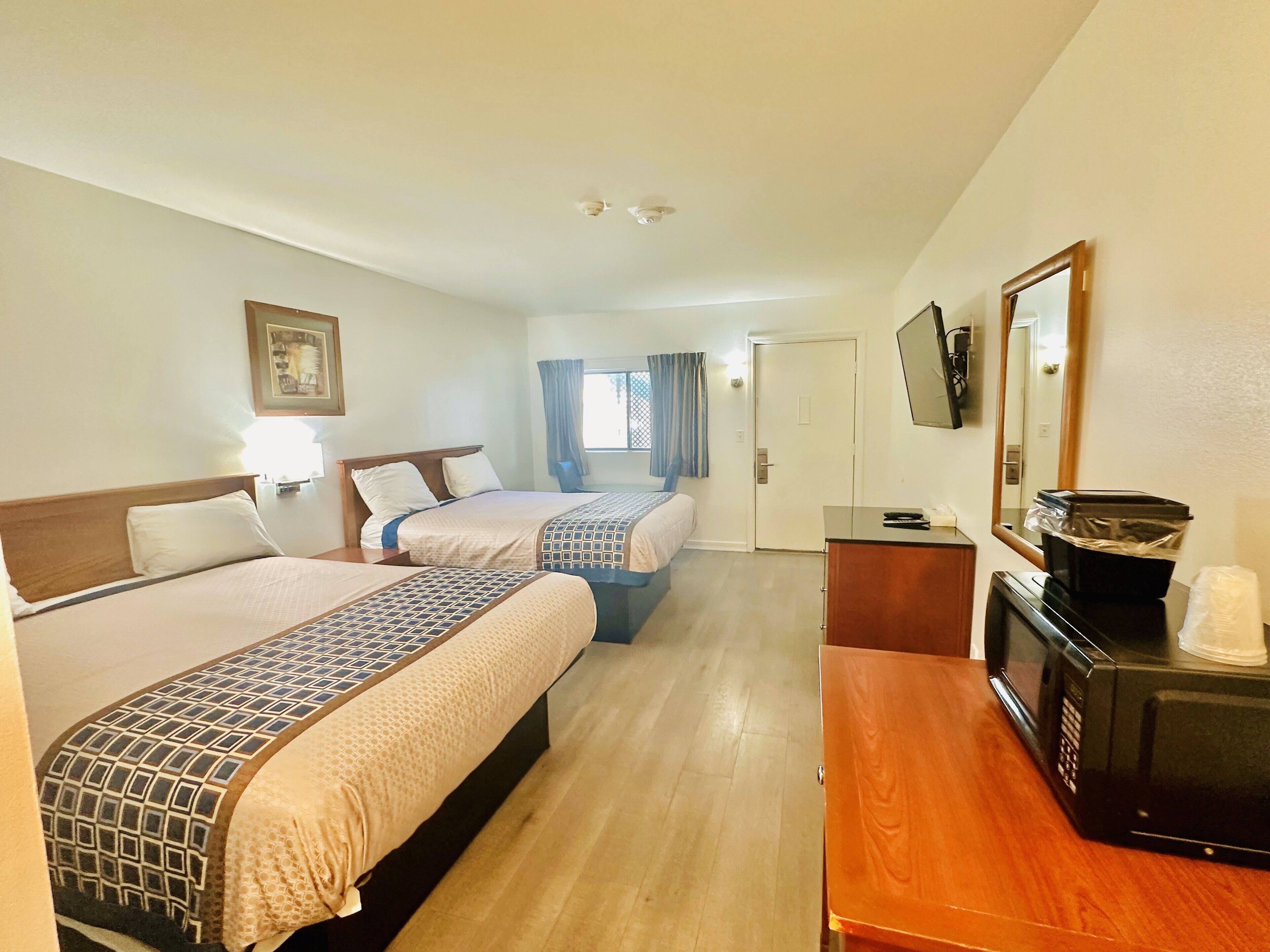 Ein Hotelzimmer mit zwei Betten, einem Holztisch, einer Mikrowelle und einem Fernseher.
