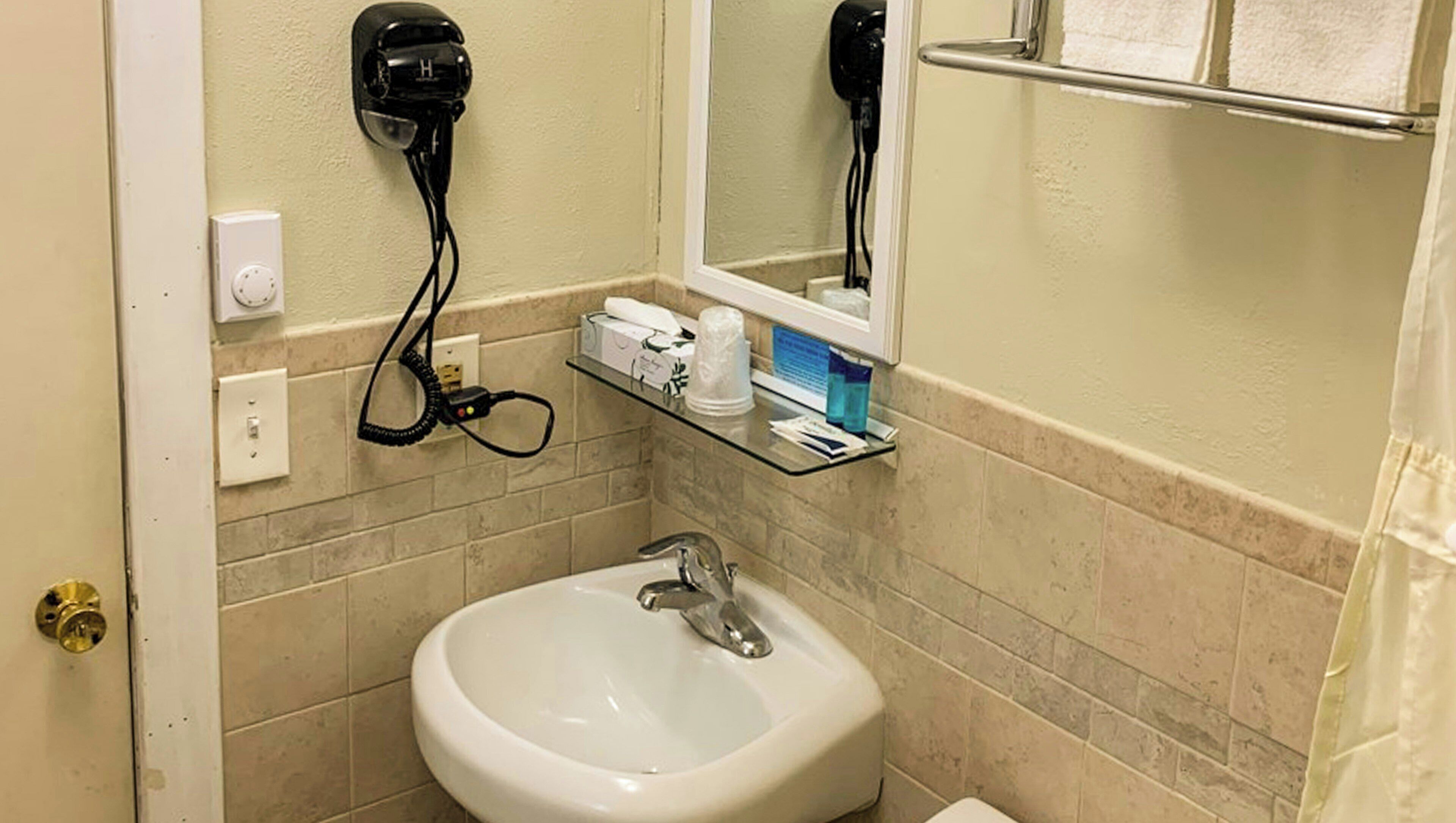 A bathroom with a sink, a mirror, a hairdryer, and toiletries on a shelf.