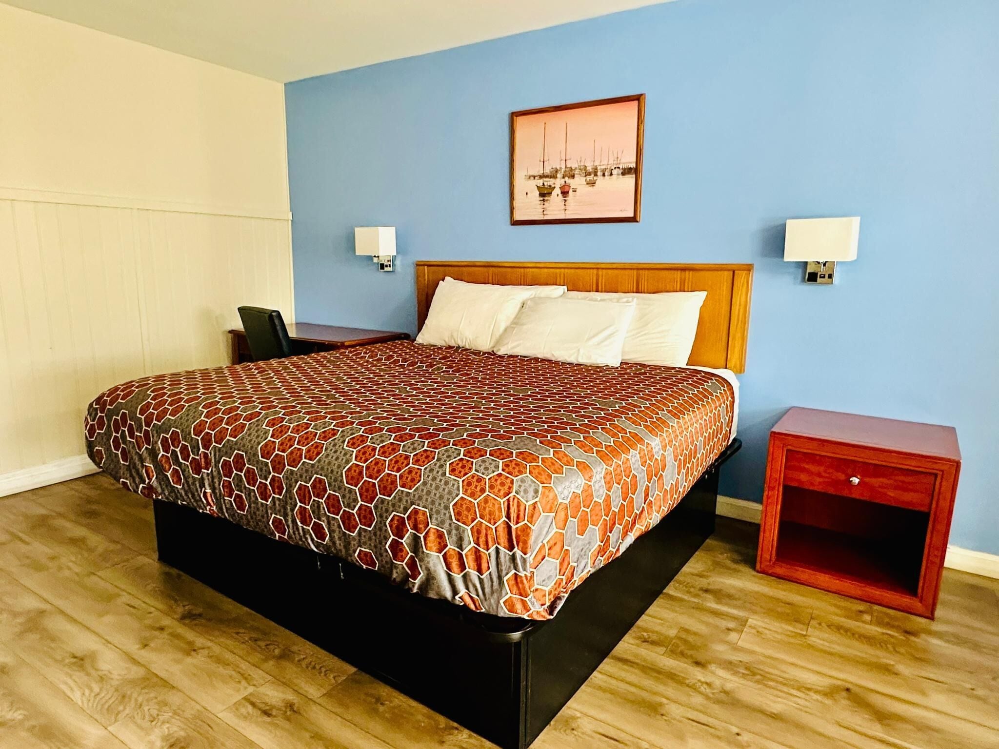 A neatly made bed with a patterned bedspread, a wooden headboard, and a small bedside table with a drawer.