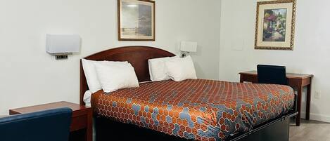A hotel room with a large bed, a desk, a chair, and two bedside tables.
