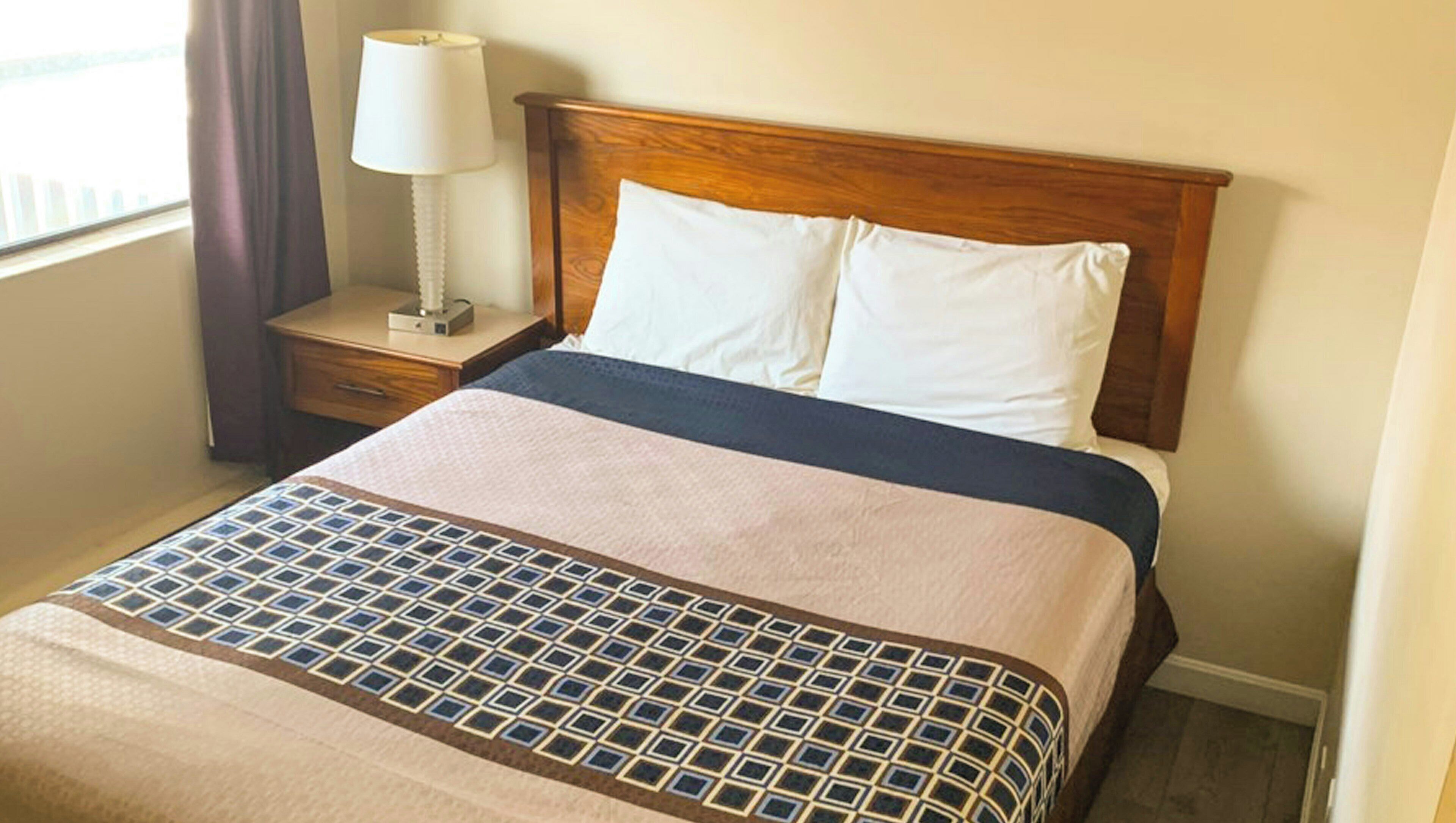 A hotel room with a bed, a nightstand, a lamp, and a window with curtains.