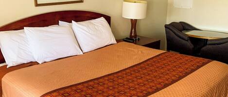 A hotel room with a bed, a nightstand with a lamp, a small table, and a chair.