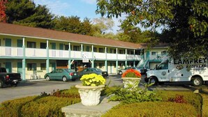 A motel with a two-story structure, a parking lot with several cars, and a truck parked outside. - Hampton Motor Inn (Hampton)