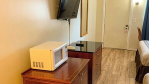 A microwave on a wooden dresser, a television on the wall, and a bed with a blue curtain. - Hampton Motor Inn (Hampton)