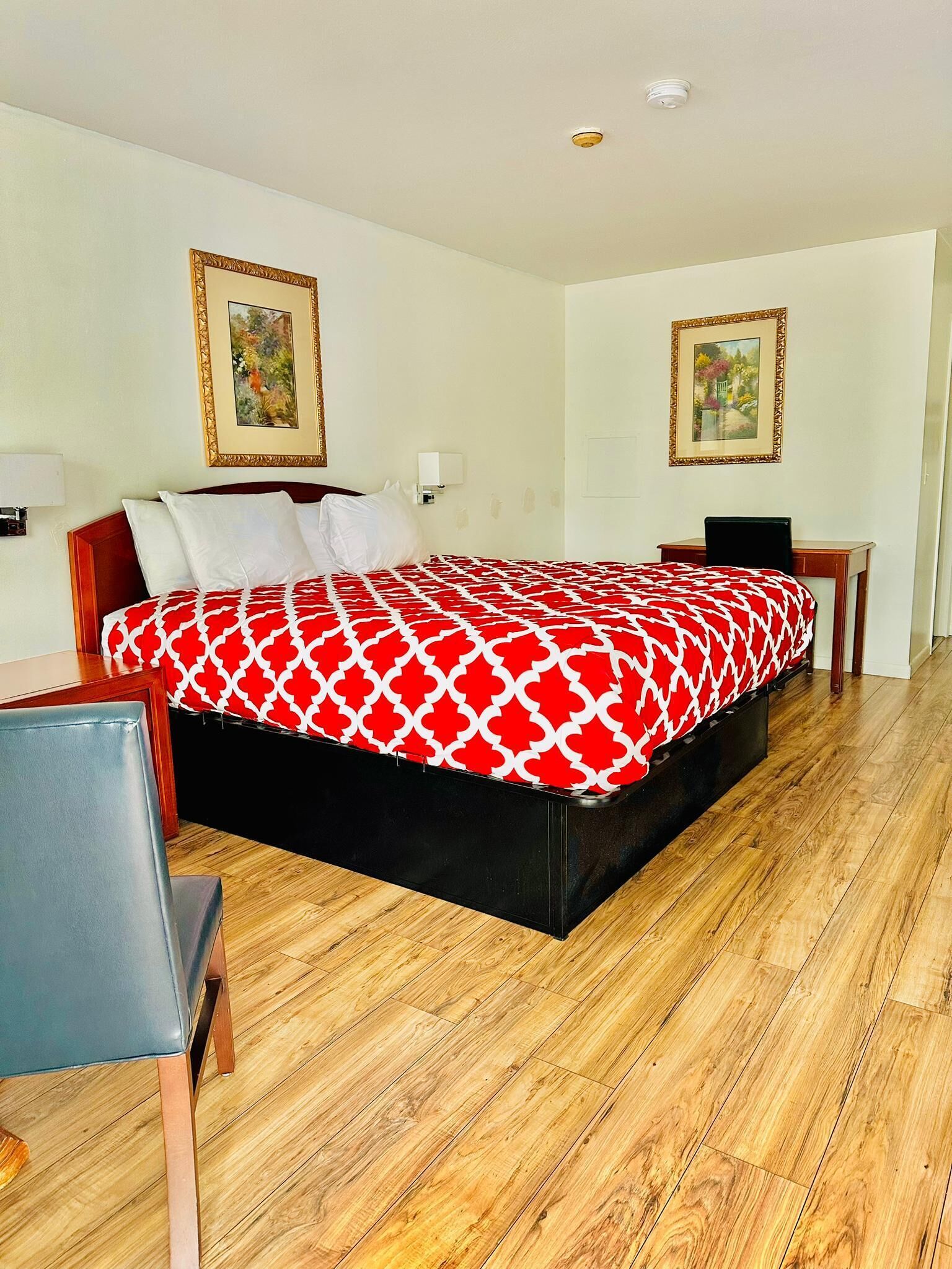 A hotel room with a large bed, a desk, and two framed pictures on the walls.