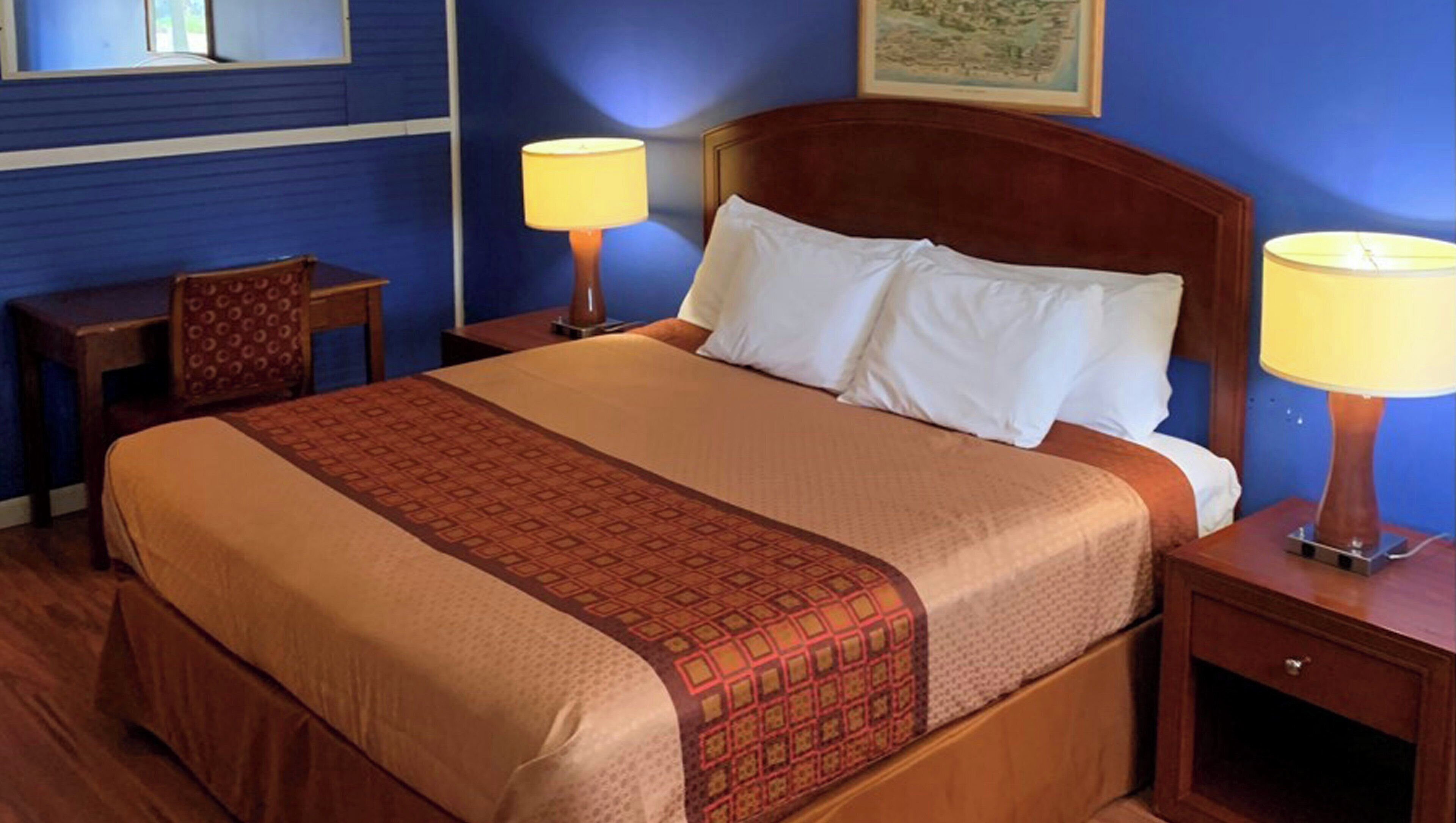 A hotel room with a bed, two bedside tables, a chair, and a wall-mounted lamp.
