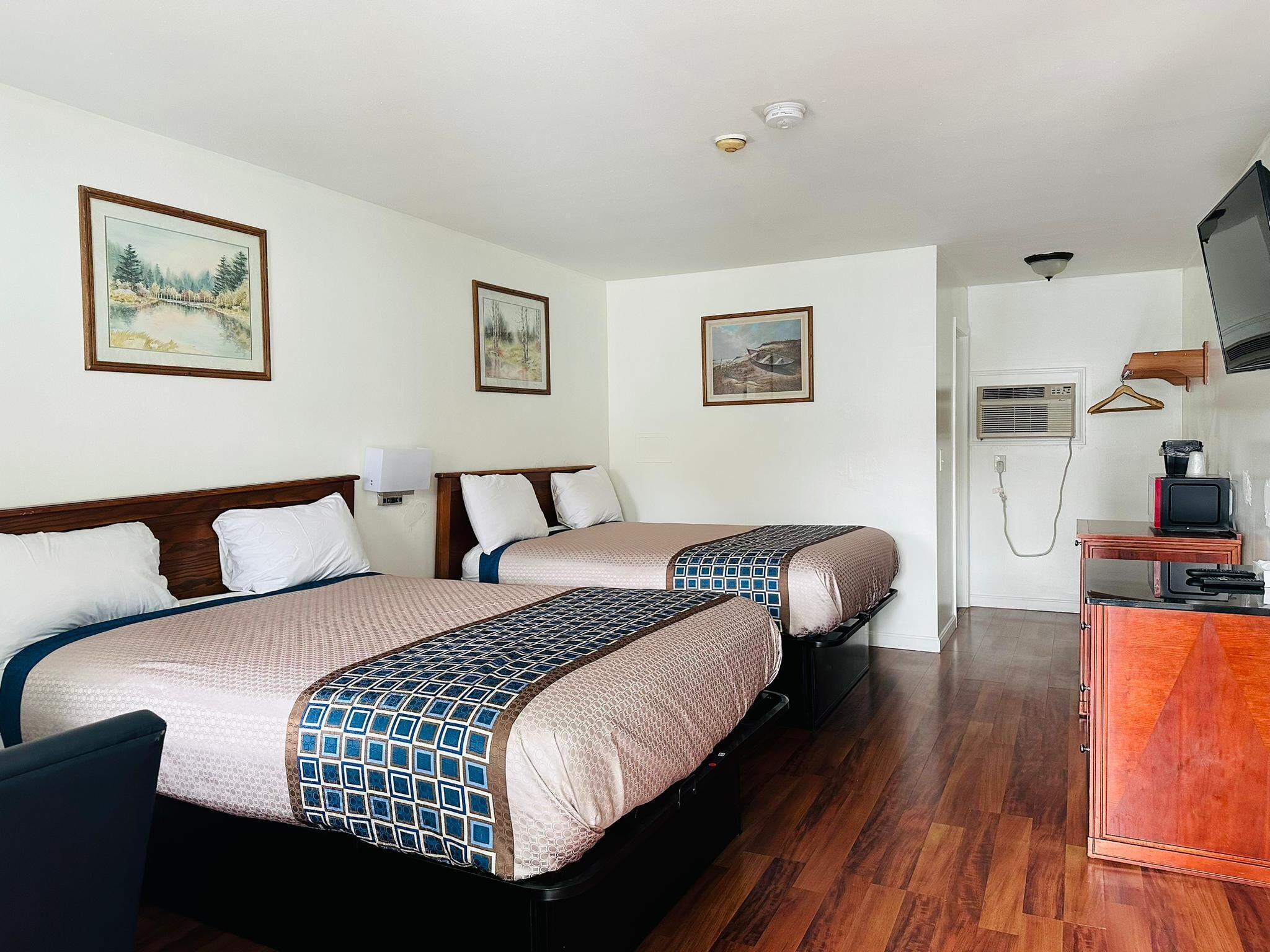 Habitación de hotel con dos camas, un aparador de madera, un televisor y un calefactor.