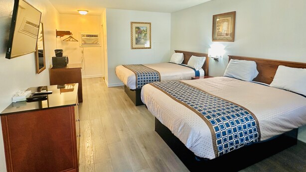 A hotel room with two beds, a desk, a mirror, and a painting on the wall. - Hampton Motor Inn (Hampton)