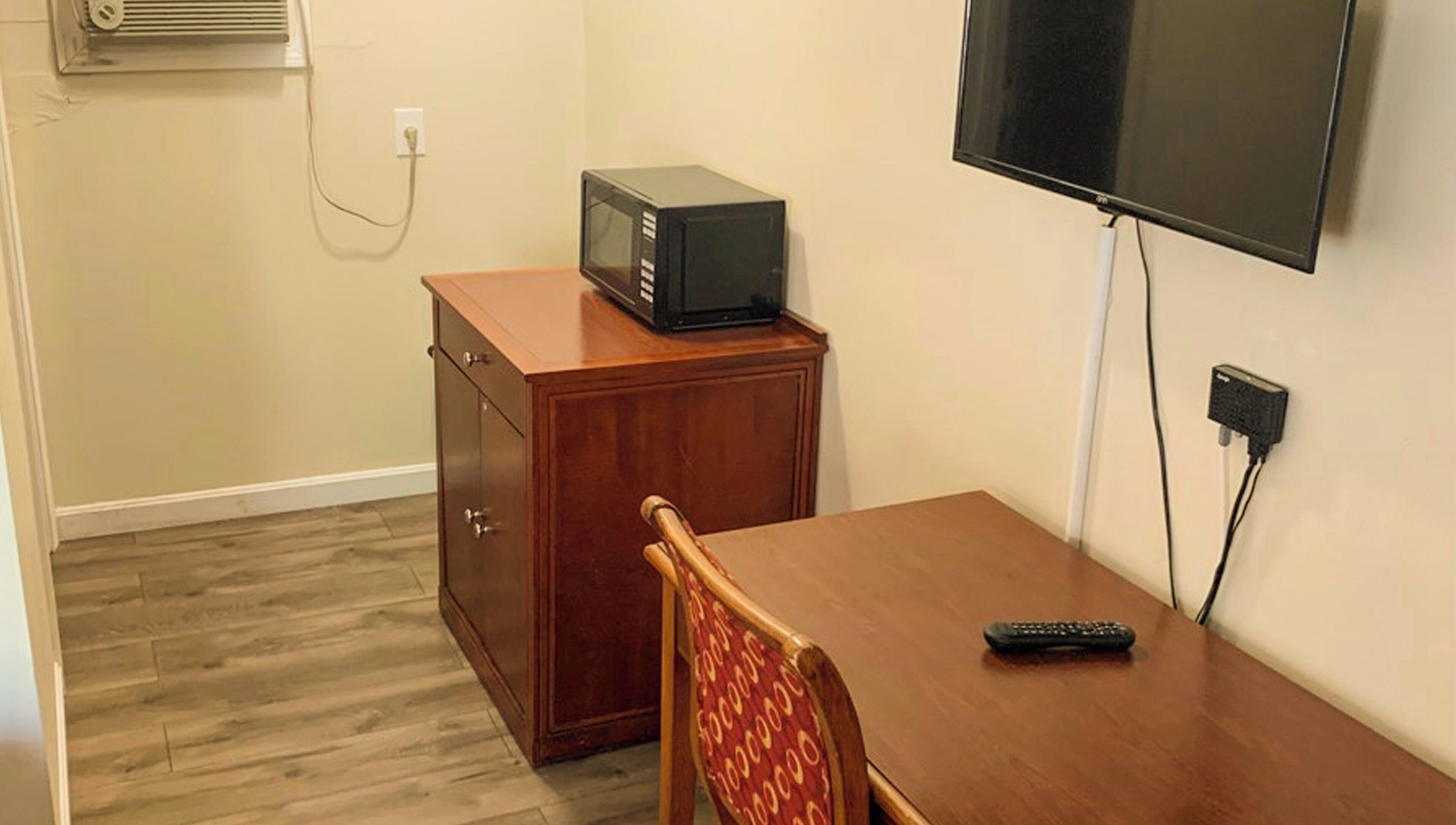 A small room with a wooden cabinet, a television mounted on the wall, a wooden table, and a chair.