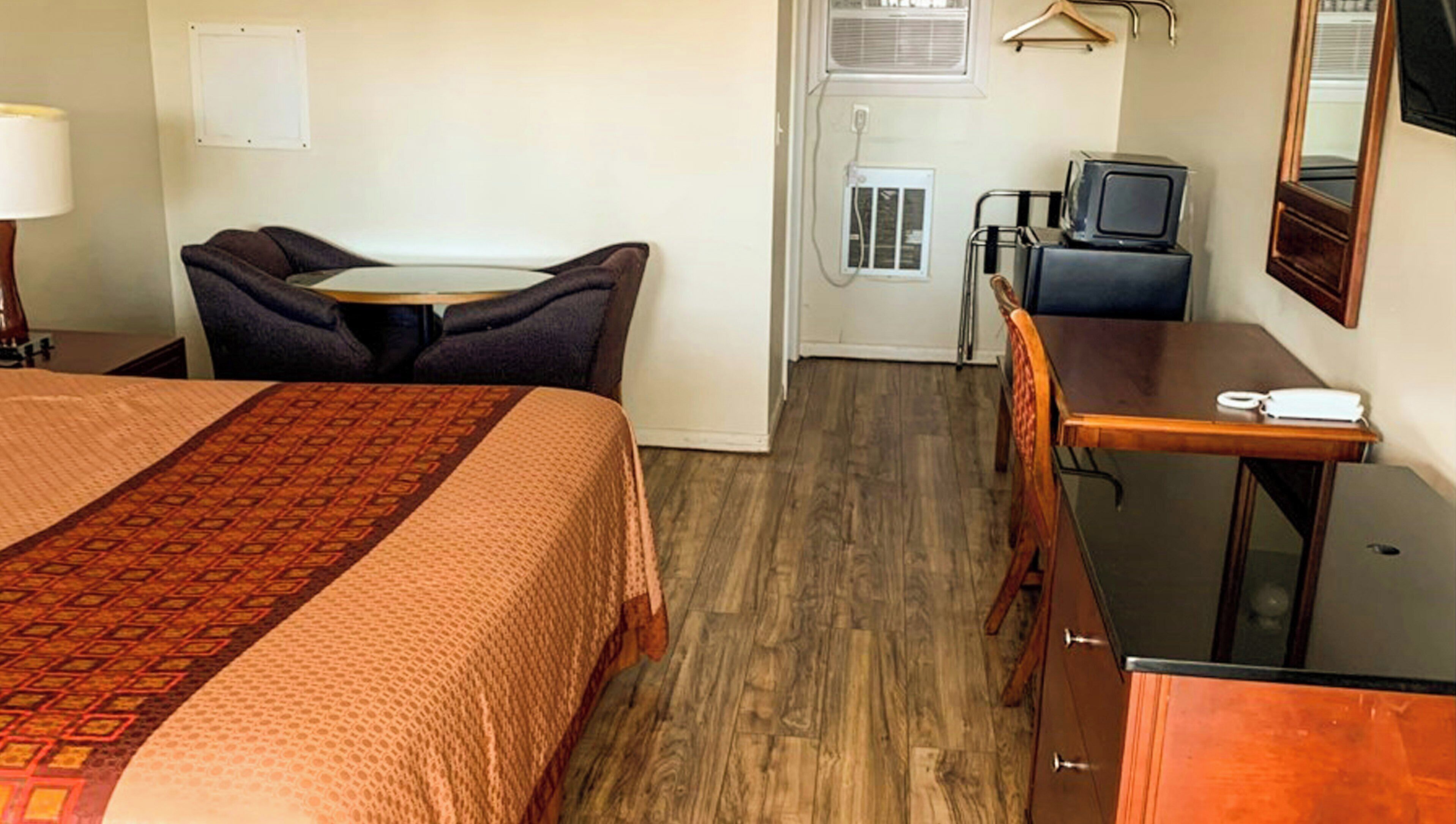A hotel room with a bed, a desk, a chair, a television, and a dresser.