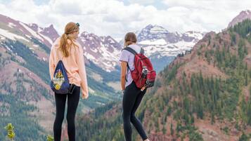 Two people standing on a mountain edge overlooking a valley with snow-capped mountains.