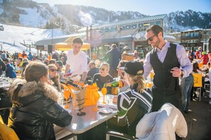 A crowded outdoor dining area with tables and chairs, surrounded by buildings and a snowy landscape. - Residences at the Little Nell (Aspen)