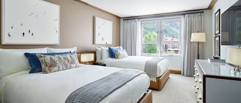 Habitación de hotel con dos camas, un escritorio y un amplio ventanal con vistas a zonas verdes y edificios.