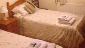 A bedroom with two single beds, each with a pillow and a folded towel. There is a nightstand with a lamp and a dresser with drawers. - Balterley Green Farm (Crewe)