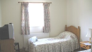 A bedroom with two single beds, a wooden dresser, a radiator, and a window with floral curtains. - Balterley Green Farm (Crewe)