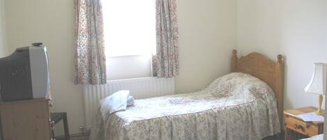 A bedroom with two single beds, a wooden dresser, a radiator, and a window with floral curtains.