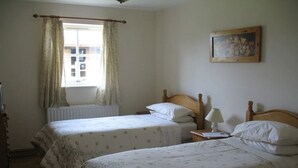 A room with two single beds, a radiator, a window with curtains, a painting on the wall, and a lamp on a bedside table. - Balterley Green Farm (Crewe)