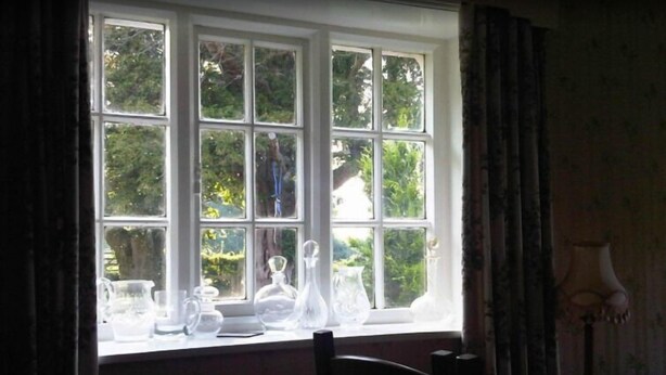 A room with a large window, a table with clear glassware, and a lamp on a side table. - Balterley Green Farm (Crewe)
