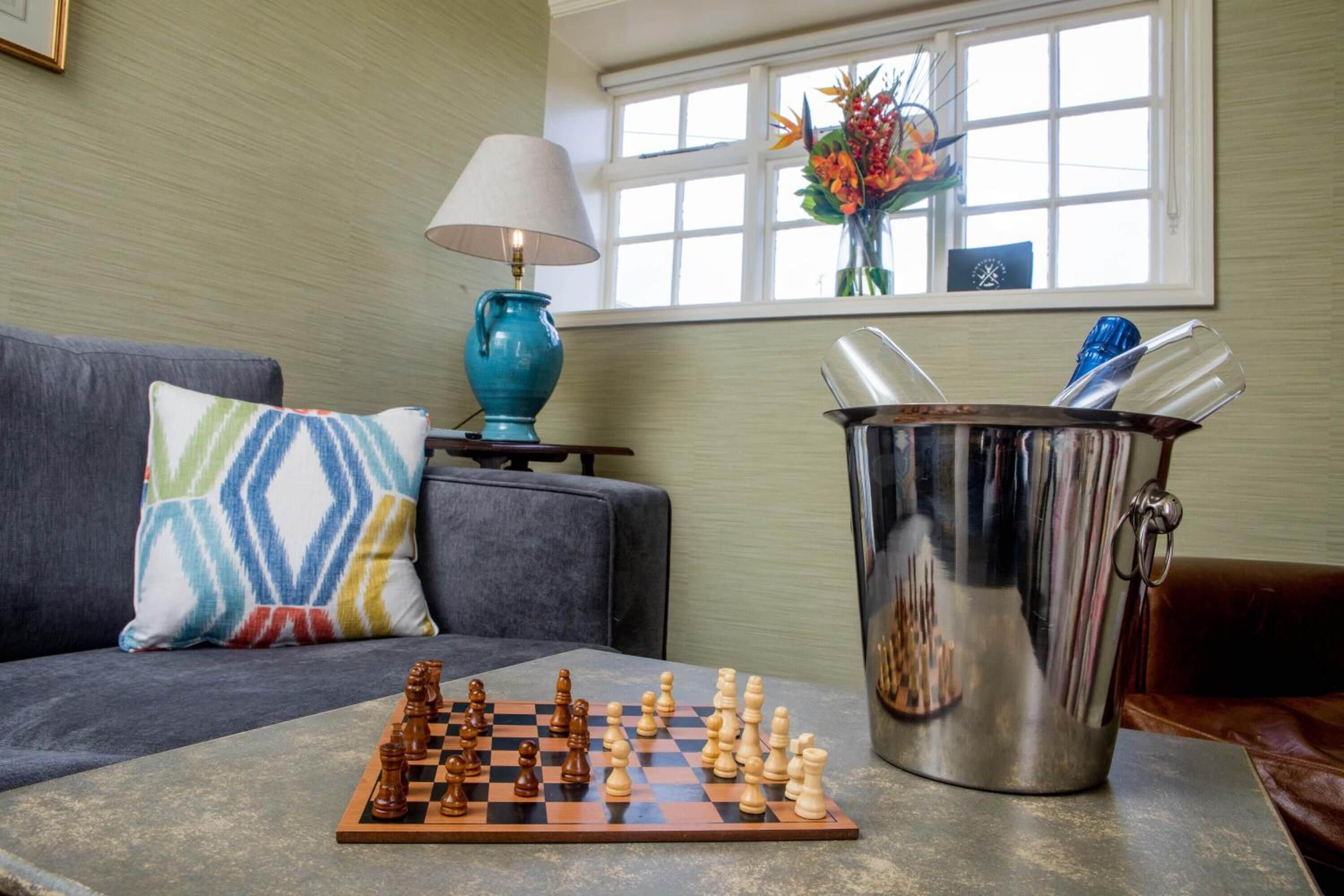 A living room with a chessboard on a table, a lamp, a vase with flowers, and a metal bucket.