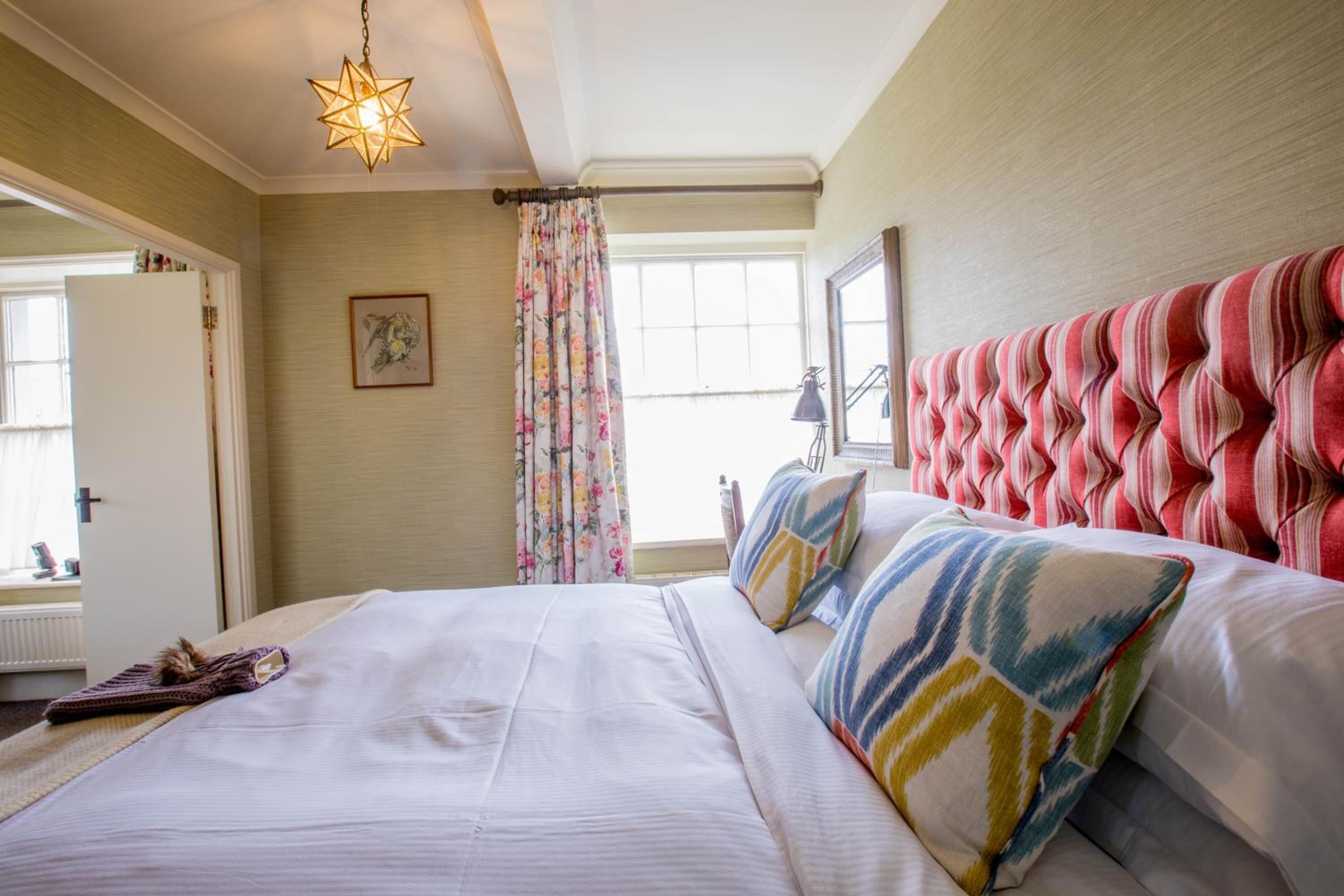 A hotel room with a large bed, a decorative star-shaped light fixture, a window with floral curtains, and a striped headboard.