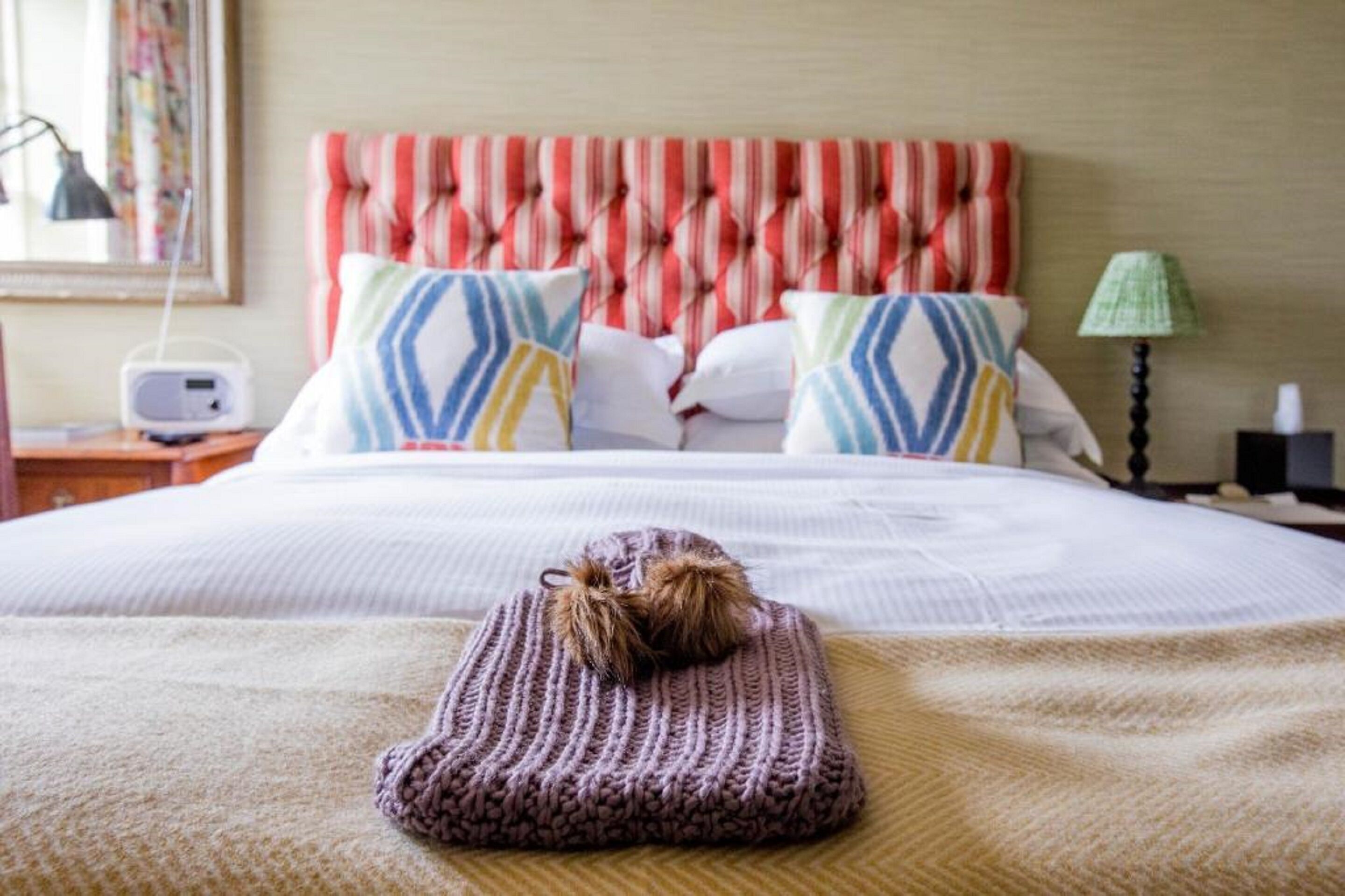 Una cama bien hecha con un cabecero a rayas, una manta de punto y almohadas decorativas.