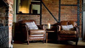 A cozy room with two leather armchairs, a small table with a candle, and exposed brick walls. - The Hawk Inn (Andover)