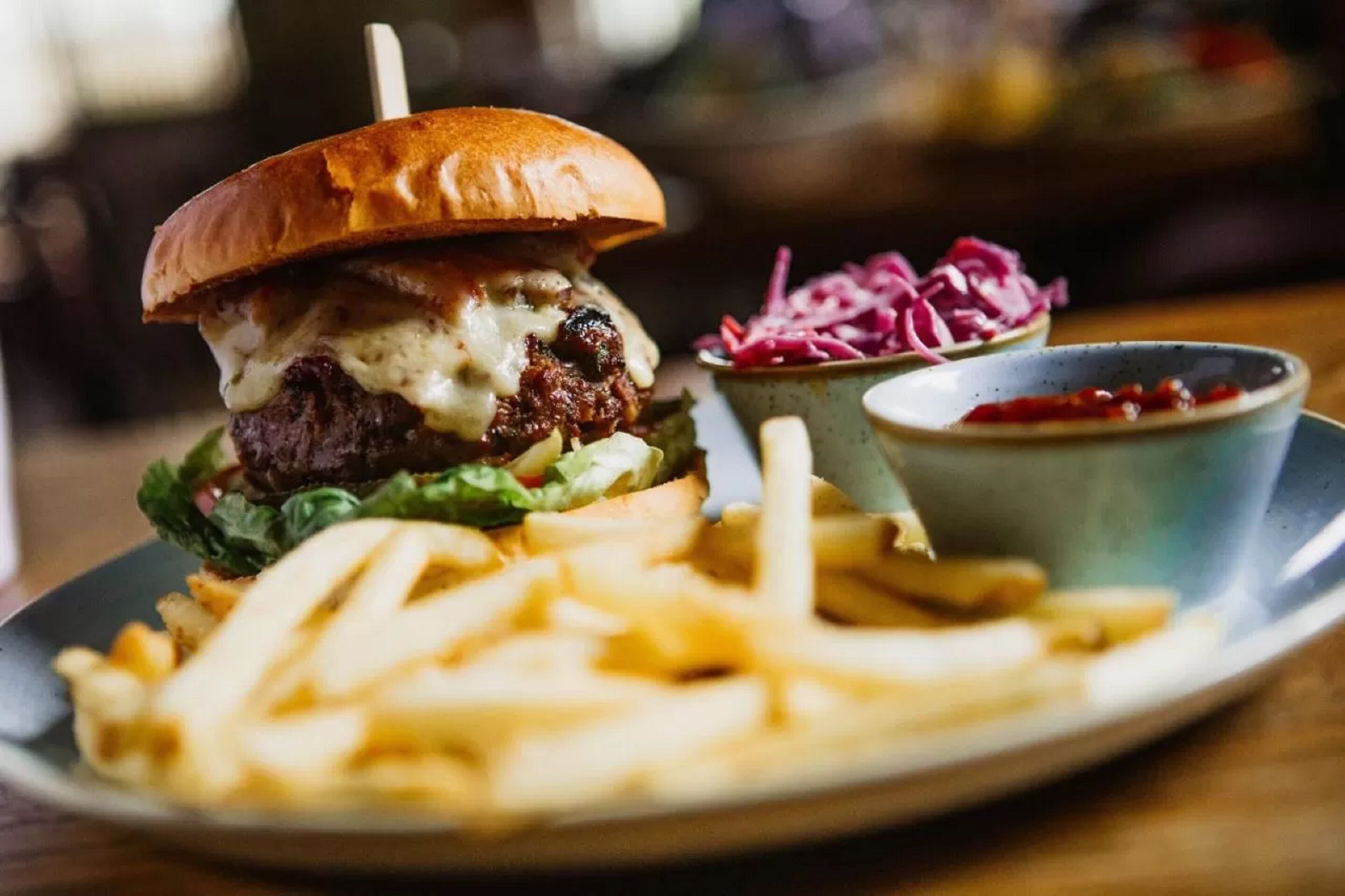 Una hamburguesa acompañada de papas fritas y ensalada de col en un plato.