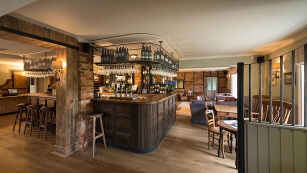 A bar area with a central island, stools, and a seating area with tables and chairs. - The Hawk Inn (Andover)