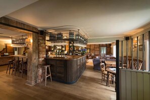 A bar area with a central island, stools, and a seating area with tables and chairs. - The Hawk Inn (Andover)